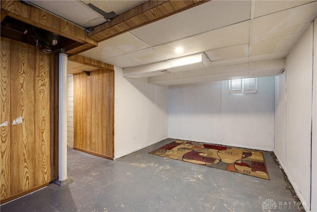 basement with a drop ceiling and wood walls