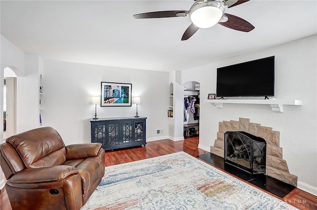 living room featuring built in shelves, dark wood-type flooring, and ceiling fan