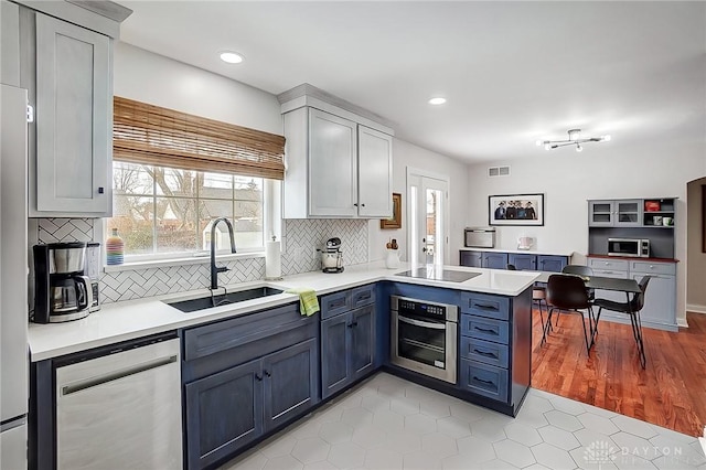 kitchen featuring blue cabinets, sink, tasteful backsplash, kitchen peninsula, and stainless steel appliances