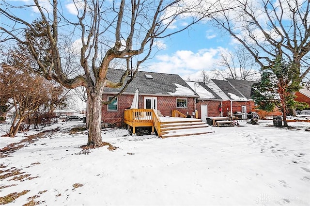 snow covered back of property with a wooden deck