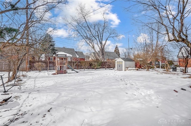 yard layered in snow featuring a playground and a storage shed