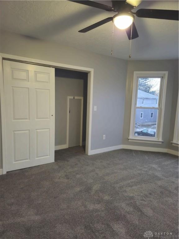 unfurnished bedroom with dark carpet, a closet, and ceiling fan