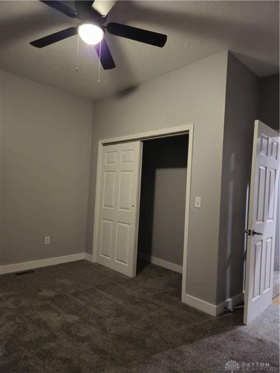 unfurnished bedroom featuring dark carpet, a closet, and ceiling fan