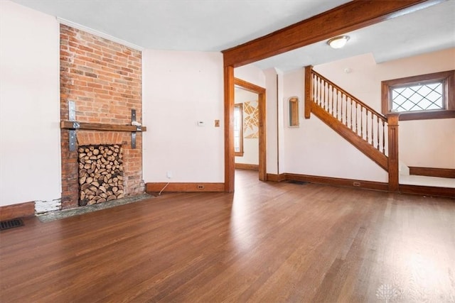 unfurnished living room with hardwood / wood-style flooring, a brick fireplace, and beam ceiling