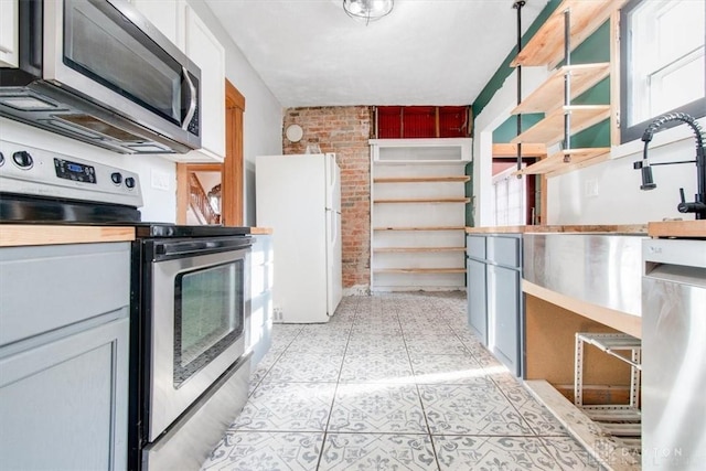 kitchen featuring white cabinets, brick wall, appliances with stainless steel finishes, and light tile patterned floors