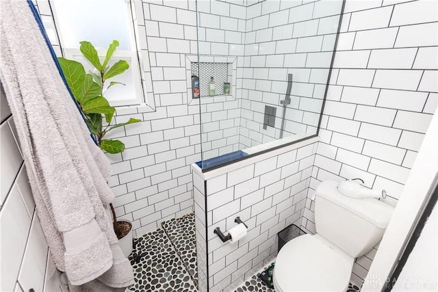 bathroom featuring a tile shower, tile walls, and toilet