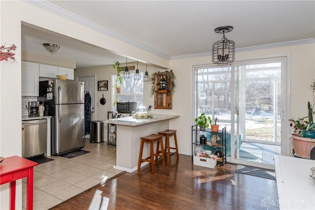 kitchen with a kitchen bar, crown molding, appliances with stainless steel finishes, pendant lighting, and white cabinets