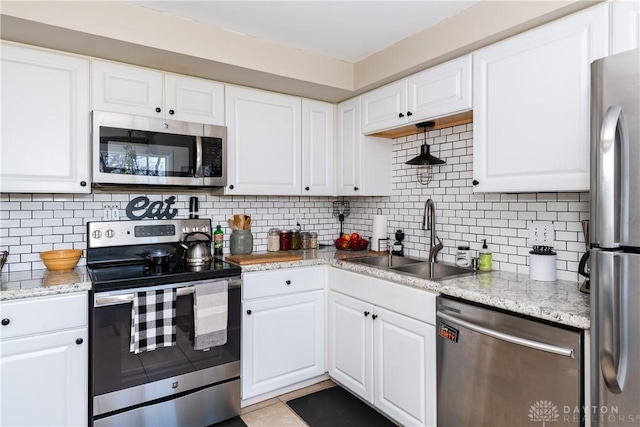 kitchen featuring sink, white cabinetry, light stone counters, stainless steel appliances, and backsplash