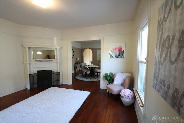 bedroom with arched walkways, dark wood-style flooring, a fireplace, and baseboards