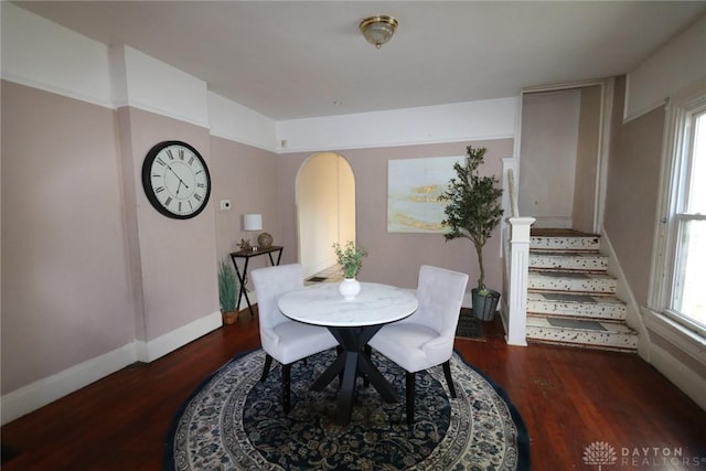 dining area featuring arched walkways, stairway, wood finished floors, and baseboards