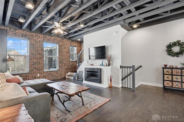 living room with beam ceiling, dark wood-type flooring, ceiling fan, and brick wall