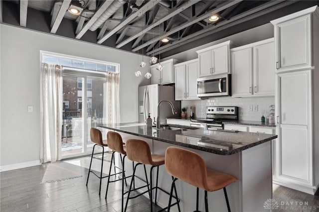 kitchen featuring sink, white cabinetry, backsplash, stainless steel appliances, and a center island with sink