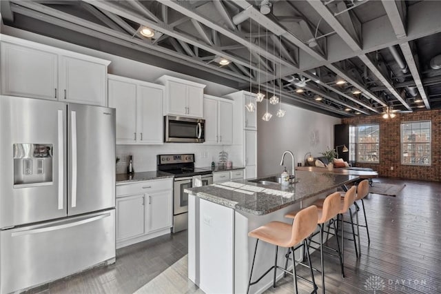 kitchen with dark stone countertops, stainless steel appliances, an island with sink, and white cabinets