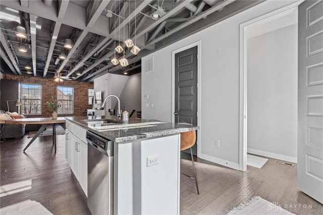 kitchen featuring stone counters, white cabinetry, dishwasher, an island with sink, and a kitchen breakfast bar