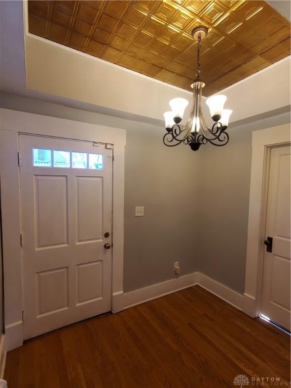 foyer with a raised ceiling, a notable chandelier, and dark hardwood / wood-style flooring