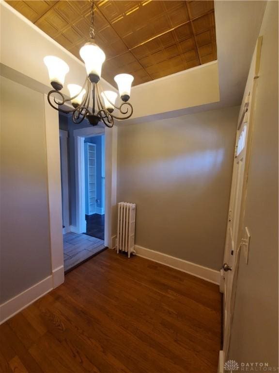 unfurnished dining area with dark hardwood / wood-style floors, radiator heating unit, a tray ceiling, and a chandelier