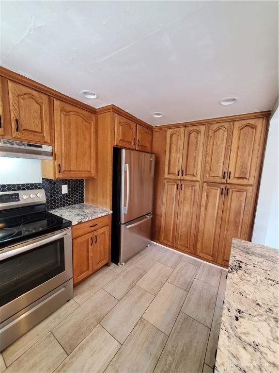 kitchen with light stone counters, stainless steel appliances, and backsplash