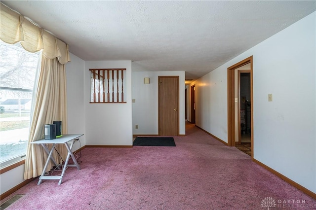 carpeted empty room featuring visible vents, a textured ceiling, and baseboards