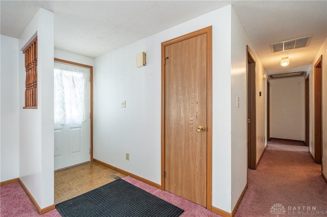 hall with a textured ceiling, visible vents, and baseboards