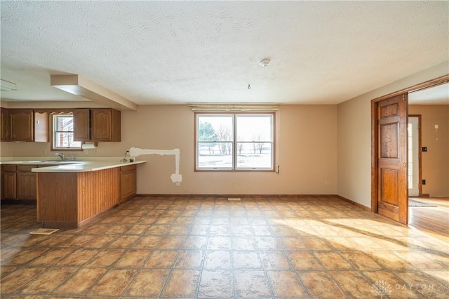 kitchen featuring a peninsula, brown cabinetry, baseboards, and light countertops