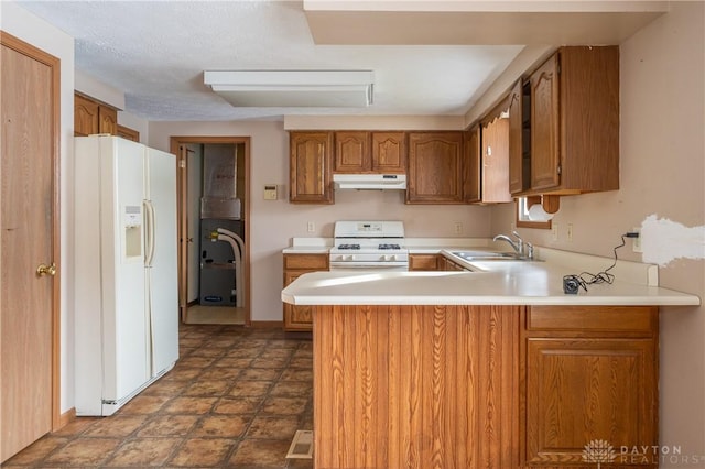 kitchen with under cabinet range hood, a peninsula, white appliances, light countertops, and brown cabinetry