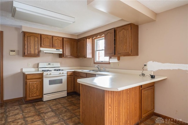 kitchen featuring under cabinet range hood, white range with gas stovetop, a sink, light countertops, and brown cabinetry