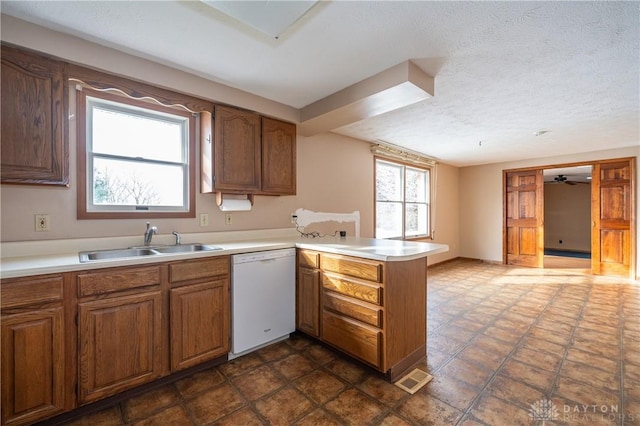 kitchen with visible vents, light countertops, white dishwasher, a sink, and a peninsula