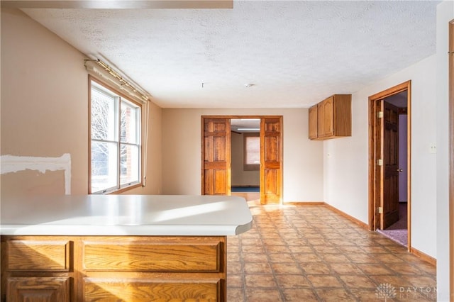 kitchen with baseboards, brown cabinetry, a peninsula, light countertops, and a textured ceiling