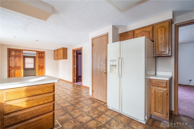 kitchen featuring a textured ceiling, light countertops, white refrigerator with ice dispenser, and brown cabinetry