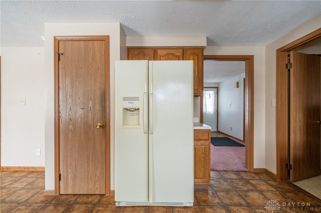 kitchen featuring a textured ceiling, light countertops, white refrigerator with ice dispenser, and baseboards