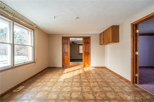 empty room featuring baseboards, visible vents, and a textured ceiling