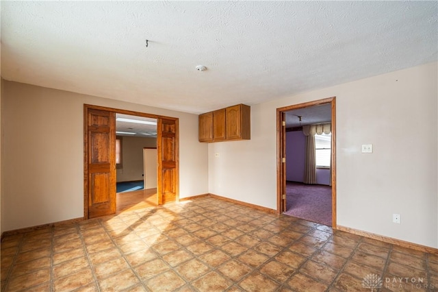 spare room featuring a textured ceiling and baseboards