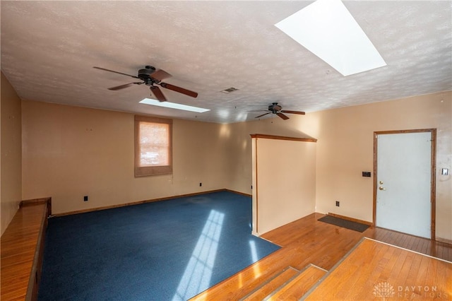 empty room featuring a skylight, visible vents, a textured ceiling, and wood finished floors