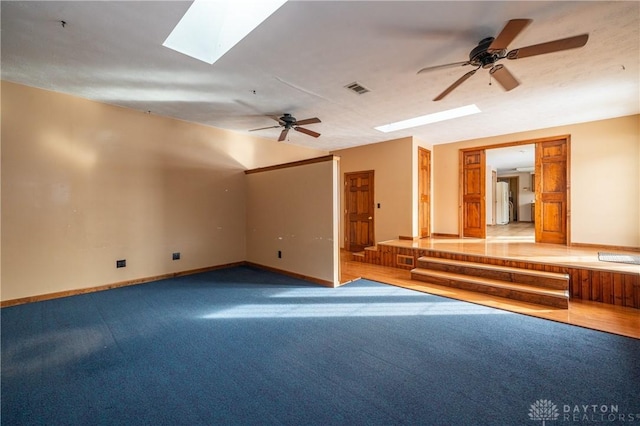 carpeted empty room with a ceiling fan, a skylight, visible vents, and baseboards