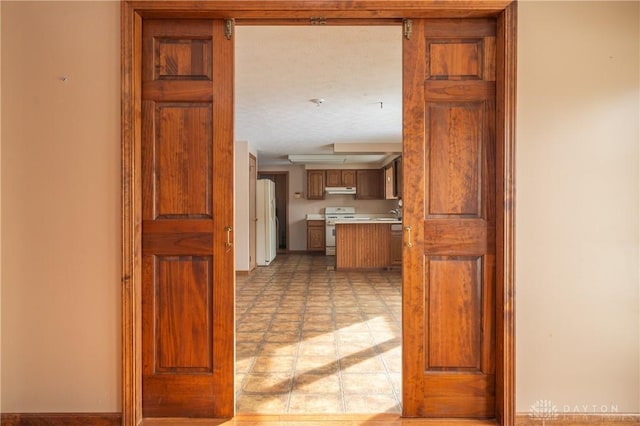 kitchen featuring a textured ceiling, under cabinet range hood, white appliances, light countertops, and brown cabinets