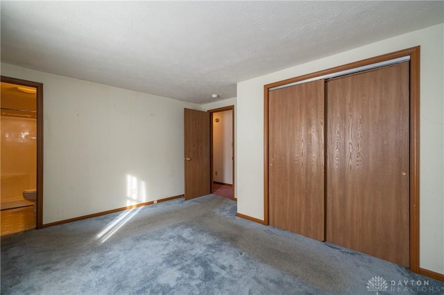 unfurnished bedroom featuring a closet, light colored carpet, a textured ceiling, ensuite bath, and baseboards