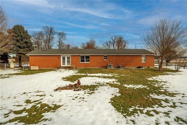 snow covered property with french doors, brick siding, and a lawn