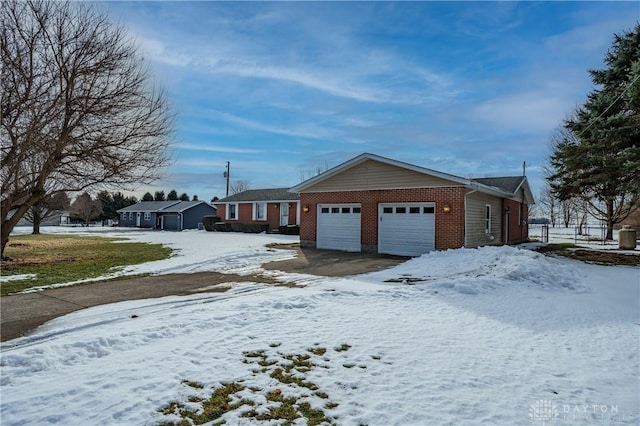 snow covered property with a garage, driveway, and brick siding