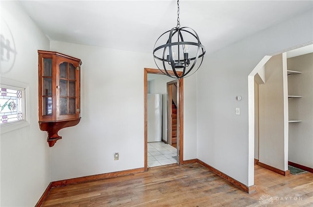 unfurnished dining area featuring built in features, a notable chandelier, and light hardwood / wood-style flooring