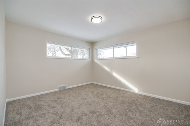 spare room featuring carpet, plenty of natural light, visible vents, and baseboards