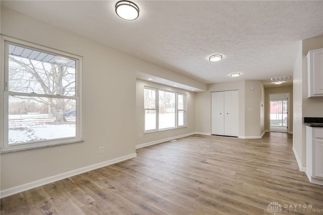 unfurnished living room with visible vents, baseboards, a textured ceiling, and light wood finished floors