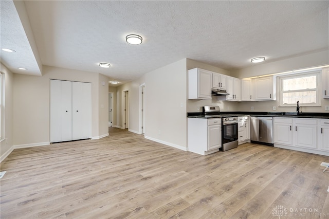 kitchen with dark countertops, light wood-style flooring, appliances with stainless steel finishes, under cabinet range hood, and baseboards