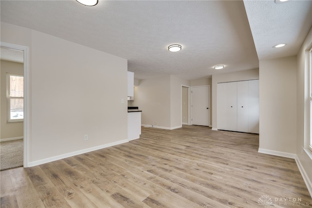 empty room featuring a textured ceiling, light wood-type flooring, and baseboards