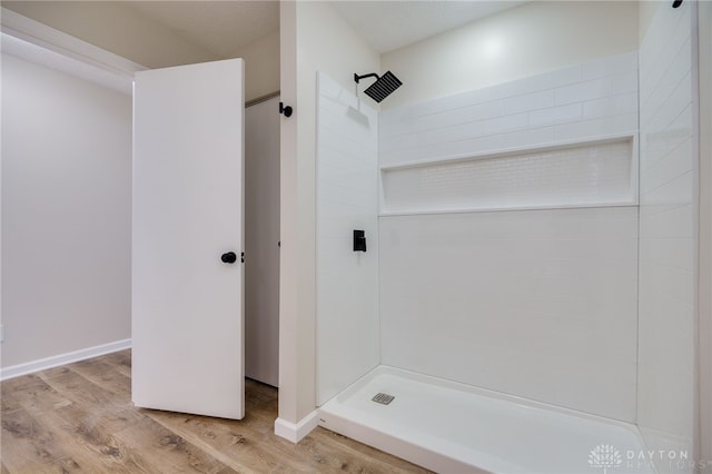 full bathroom featuring a tile shower, baseboards, and wood finished floors