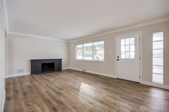 unfurnished living room with crown molding, a fireplace, visible vents, and wood finished floors