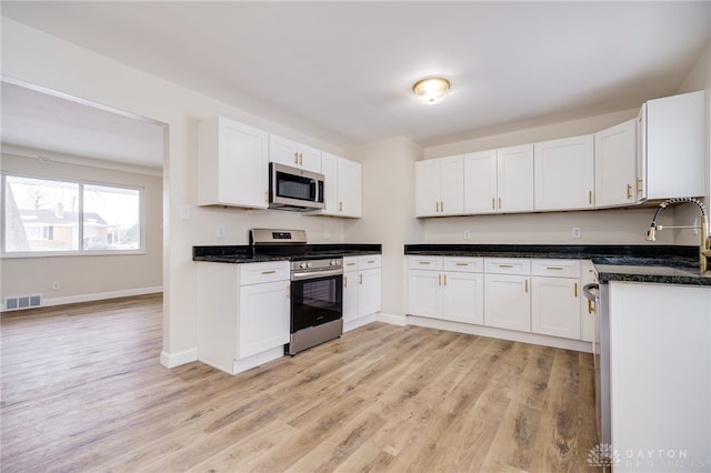 kitchen with stainless steel appliances, visible vents, light wood-style flooring, white cabinets, and a sink