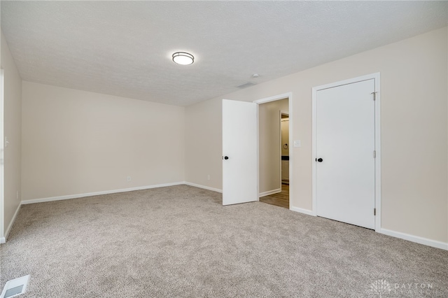 carpeted spare room with baseboards, visible vents, and a textured ceiling