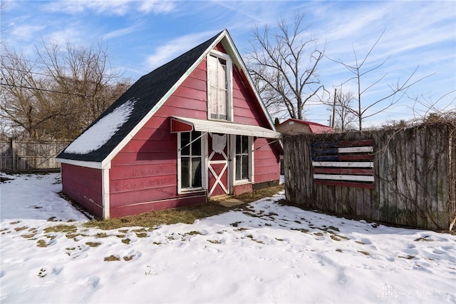 snow covered structure featuring an outdoor structure, a barn, and fence