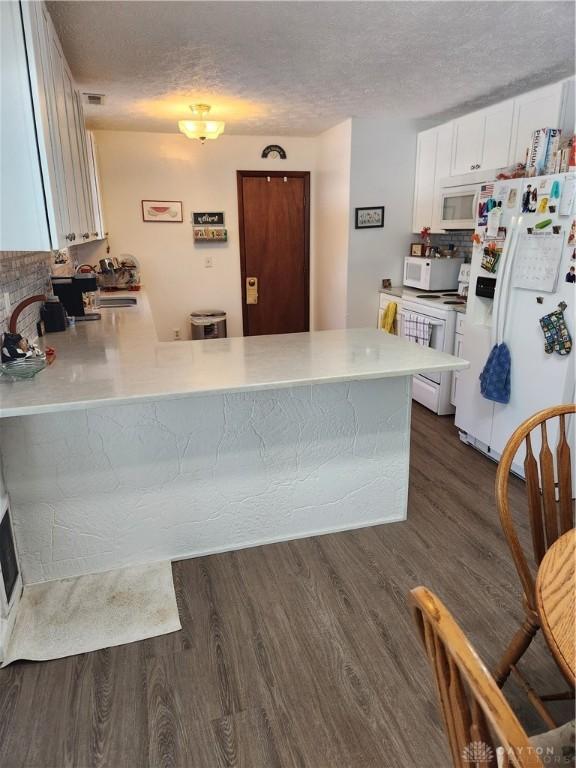 kitchen featuring white cabinetry, white appliances, dark hardwood / wood-style floors, and kitchen peninsula