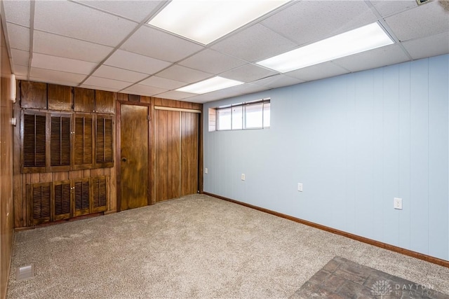 basement with a paneled ceiling, wooden walls, and carpet floors